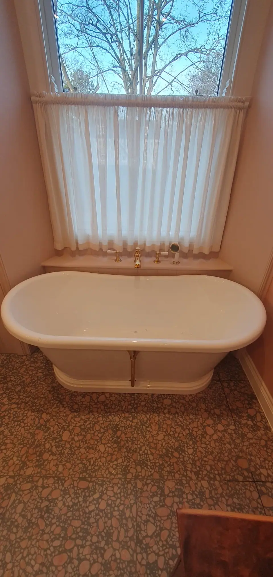 Freestanding white bath with brass taps beneath a sash window