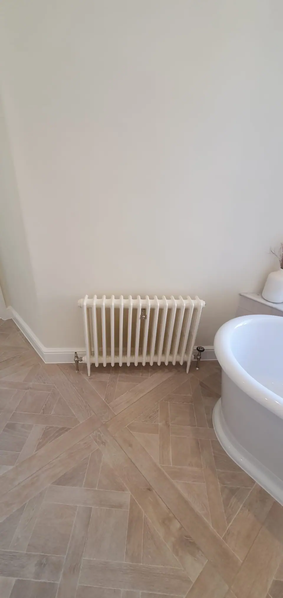 White column radiator with chrome valves on a herringbone floor
