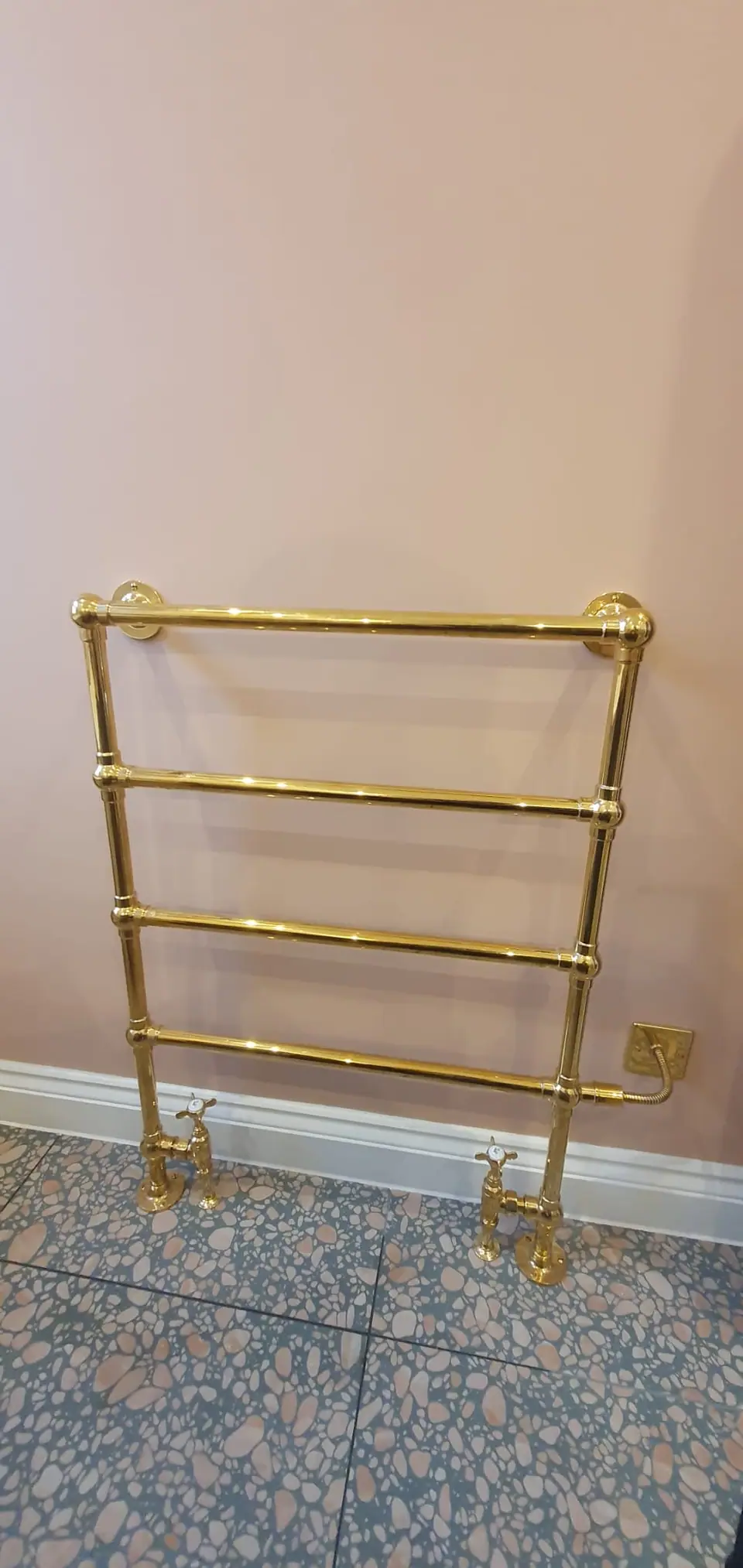 Brass heated towel rail with traditional valves, wall-mounted in a bathroom